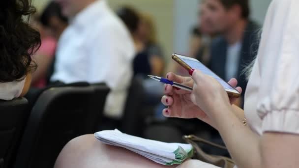 Girl with a pen writes something in notepad and scrolls the screen of mobile phone — Stock Video