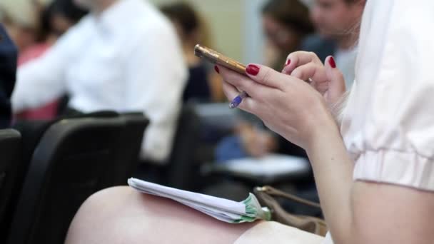 Chica con bloc de notas se sienta en la sala de conferencias y se desplaza por la pantalla, primer plano de las manos femeninas están escribiendo sms — Vídeos de Stock