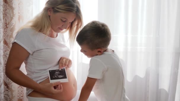 Nyfiken pojke intresserad mage mor som innehar i vapen foto av ultraljud scan — Stockvideo