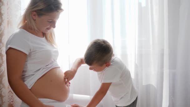 Niño pequeño acariciando y tocando el dedo a lo largo del vientre de la mujer embarazada en el interior — Vídeos de Stock