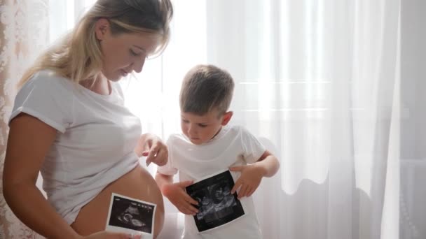 Young mother with sweet child watching photo sonography at home on background of white curtains — Stock Video