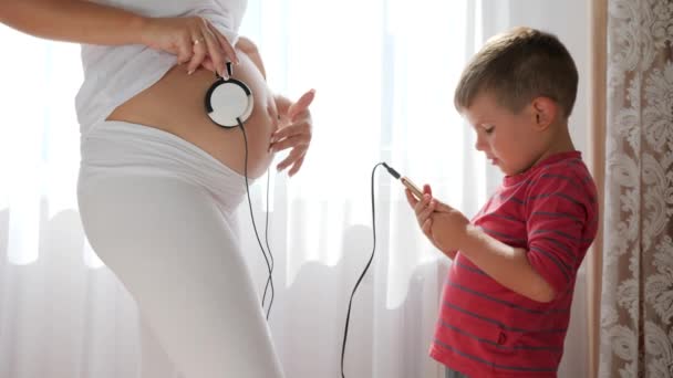 Donna incinta dà musica al bambino nella pancia attraverso le cuffie, il telefono cellulare nelle mani del bambino accanto — Video Stock