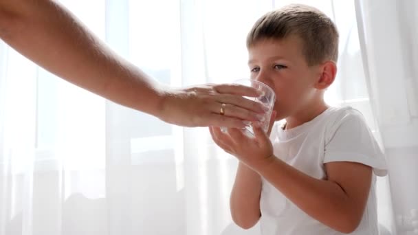 Dulce niño bebe agua mineral de vidrio transparente en el interior en luz natural iluminada — Vídeo de stock