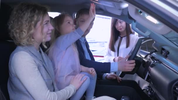 Покупка семейных автомобилей, молодая пара с симпатичной девочкой ребенка говорить о покупке автомобиля с менеджером азиатской женщины, сидя в салоне в автоцентре — стоковое видео