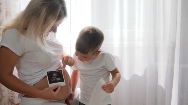 Jeune mère enceinte avec enfant doux regardant l'échographie photo à la maison dans la lumière naturelle brillante — Video