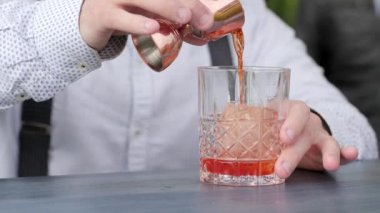 Barmen bar masasına buz koyuyor, barmen buzla bardağa meyve suyu dolduruyor.,