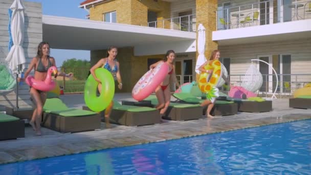 Jóvenes mujeres atractivas amigos en trajes de baño con anillos inflables saltar en el agua azul de la piscina mientras se relaja en el descanso del complejo de verano — Vídeos de Stock