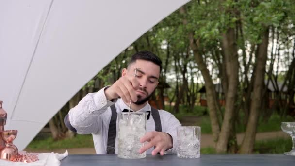 Бармен перемішуючи кубики льоду ложка на природі, склянка з льодом на барній стійці, бармен робить охолоджуючий напій свіжим повітрям, сервіс заходу — стокове відео