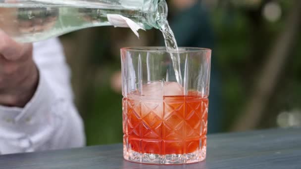 Barman añade alcohol al hielo en la mesa de bar al aire libre, barkeeper vierte licor frío en vidrio con hielo , — Vídeos de Stock