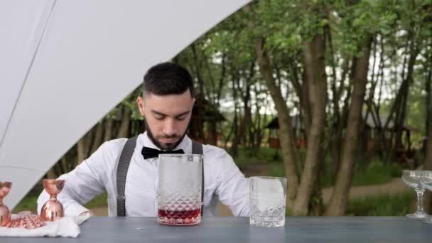 Portret barman voegt ijs toe aan glas drank op bar teller, barman doet ijs in glas met alcohol en servet, — Stockvideo