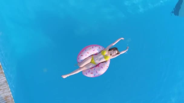 Repos d'été, fille heureuse en maillot de bain nager à l'anneau gonflable au bord de la piscine dans une station balnéaire coûteuse pendant le congé, relevé aérien — Video