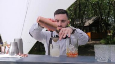 Barmen bardağa likör dolduruyor, barmen kokteyli filtreden hazırlıyor.