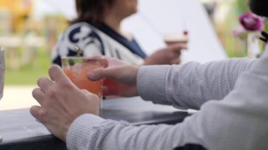 Yazlık terasta kafe, müşteriler içkileri bağışlıyor, barmen bardakta renkli kokteyl yapıyor, barmen barın arkasında.