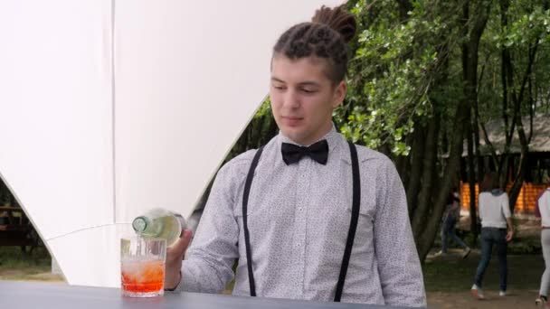 Barkeeper macht Mixgetränk auf Naturhintergrund, Bararbeiter füllt es in Glas mit Eiswürfeln — Stockvideo