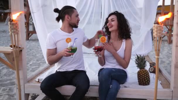 Couple drinking colored cocktail on beach an exotic vacation, cocktail party, bungalow on beach, background tropical fruits and burning torches — ストック動画