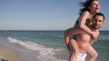 Erkeklerin sırtına atlayan mutlu bir kız, yaz tatilinde aşık bir çift, rüzgâr saçlarını, tropiklerini okyanus kıyısında geliştiriyor.,