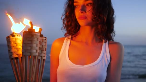 Portrait femelle tenant flambeau, feu ardent, fille aux cheveux bouclés regardant dans la caméra, îles tropicales, sur fond océan — Video