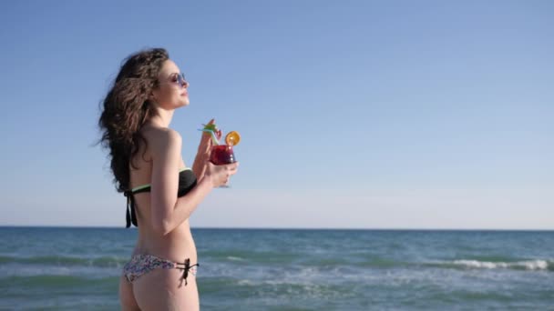 Sexy kobieta z kręconymi włosami napoje kolorowy koktajl, Portret uśmiechniętej dziewczyny na plaży, błyszczące tło morza, — Wideo stockowe