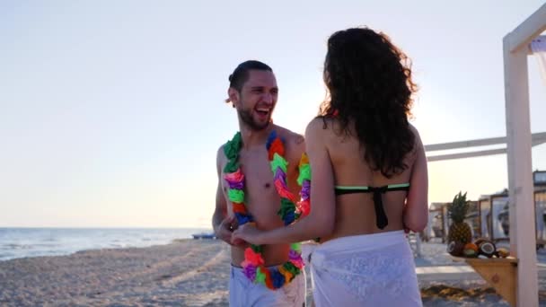 Strandparty in Zeitlupe am Wasser, verliebter Sommerurlaub am Meer, Blumenkränze am Hals eines jungen Paares, — Stockvideo