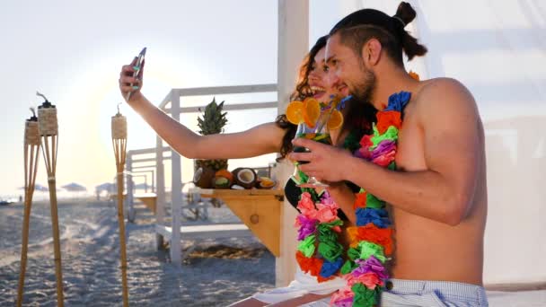 Пара з квітами вінок на шиї, сфотографована на гаджеті, селфі хлопець і дівчина з екзотичного курорту , — стокове відео