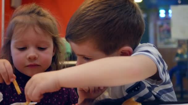 Enfants actifs et amusants jouent avec le repas dans un café de restauration rapide, enfant mâle essuie son visage avec une serviette, beau frère et soeur ont collation — Video