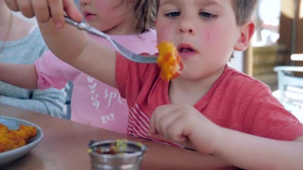 Chlapec a dívka mají chutnou večeři v restauraci, Muž dítě jí vidličku se smaženými kuřecími nugetami s omáčkou, Krásný bratr — Stock video