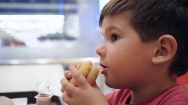 İtaatsiz çocuk hamburgeri ısırır ve onunla oynar, güzel bebek maması, hamburger ve patates kızartması oğlu için.,