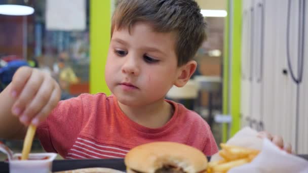 Hamburger és sült krumpli a fiúnak, Olajos ételek az iskolai menzán ebédre, Kisfiú étvággyal eszik — Stock videók