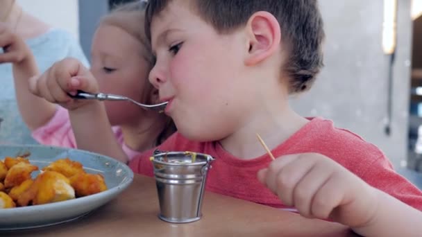 Чоловіча дитина їсть виделку зі смаженими курячими серветками з соусом, хлопчик і дівчинка вечеряють в ресторані , — стокове відео