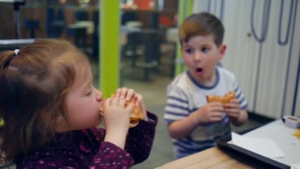 Finom hamburger és sült krumpli mártással kislánynak és fiúnak, vidám gyerekek játszanak étkezés gyorsétterem kávézó, Gyönyörű testvér és testvér — Stock videók