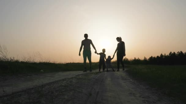 Lycklig familj på promenad i skogen slow-motion, pappa, mamma och två söner gå på väg till fältet i motljus, Silhuetter av familjen går till kameran — Stockvideo