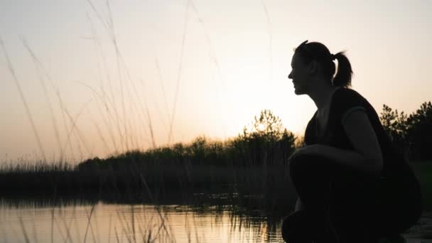 Ευτυχισμένο θηλυκό κάθεται κοντά στο ποτάμι από κοντά, το ηλιοβασίλεμα, γυναίκα κάνει βουτιά στο νερό, επιβράδυνση γυρίσματα, — Αρχείο Βίντεο