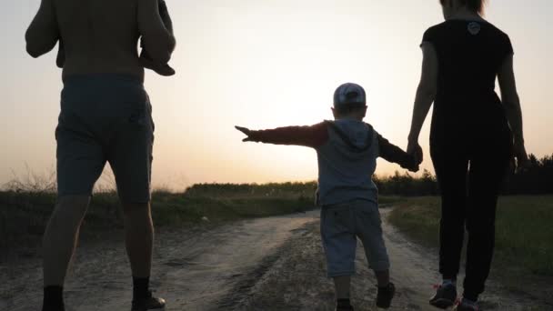 健康的父亲肩负着一个儿子，母亲牵着二儿子的手，回头看，背光下的全家福, — 图库视频影像