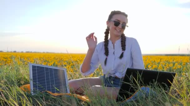 Energiesparende Technologie, Mädchen spricht auf Laptop mit Solarbatterie auf Sonnenblumenfeld, junge Frau wendet Solarzelle an — Stockvideo