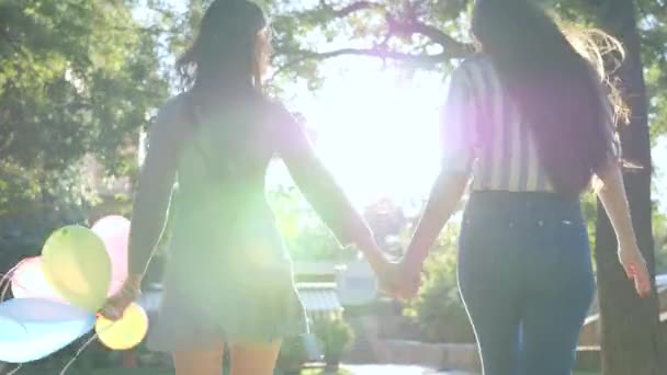 Jolies petites amies heureuses s'amusent et courent avec des ballons colorés dans le parc, des émotions heureuses dans le rétroéclairage — Video