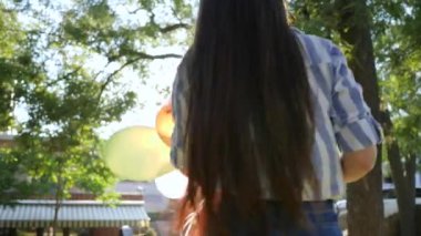 happy girlfriends spinning holding hands with colorful balloons and smiling on background green trees