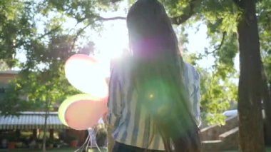lucky girls holding hands whirling with colorful balloons having fun on background green trees, emotions