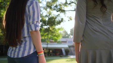 Arka planda Lgbt sembolüyle el ele tutuşan iki kız parkta yeşil ağaçlar, dışarıda dikiz manzarası