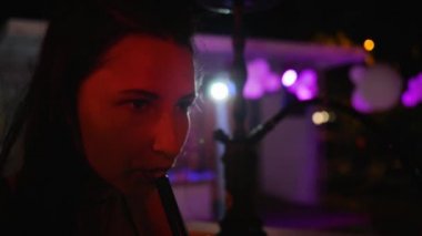 Güzel bir kadın gece partisinde tütünün tadını içine çeker. Kapalı çekimde mutlu bir kız ağır çekimde duman solur.