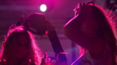 Neşeli içkilerle gülümseyen kızlar gece kulübünde eğleniyor, gece dans ederken içen mutlu kadınlar.