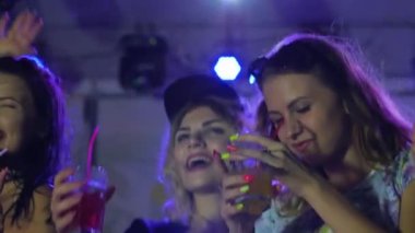 Kokteyl partisi, kızlar partilerde içeceklerle dans ediyor lumiere ışıklarında, disko kulübünde genç kadınlar, çok sayıda kadın.