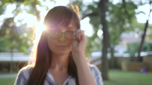 Close-up girl wears stylish eyeglasses in backlight and smiling on camera — Stock Video