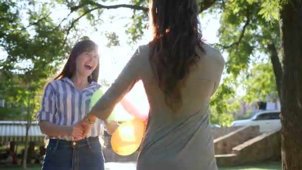 Émotions dans le contre-jour, petites amies heureuses tenant les mains filant avec des ballons colorés dans le parc sur les arbres de fond — Video