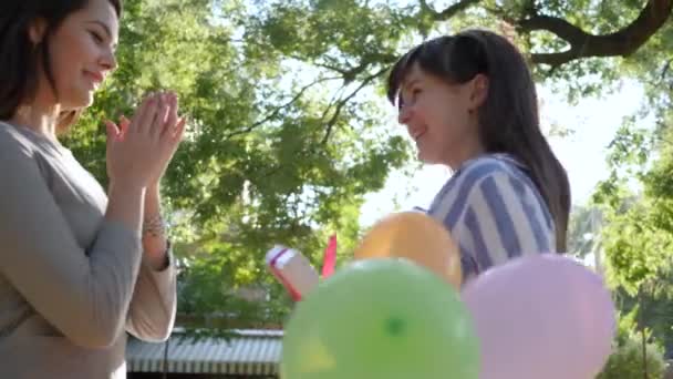 Chica con globos de colores dando regalos y abrazando a la novia al aire libre en el parque, emociones — Vídeo de stock
