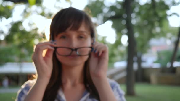 La femmina felice si mette occhiali eleganti e sorride a macchina fotografica a parco, primo piano — Video Stock