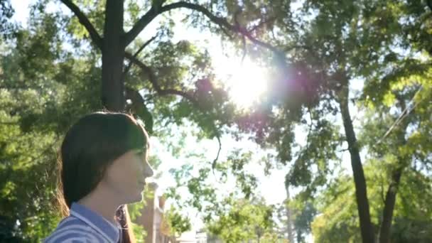 Piuttosto femminile beve acqua minerale fredda da bottiglia di vetro e sorride all'aperto in controluce su alberi verdi di sfondo — Video Stock