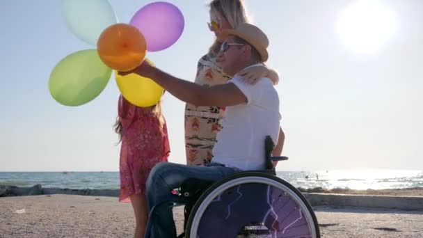 Allegra mamma, figlia con palloncini e papà in retroilluminazione, bambina, madre e padre disabile — Video Stock