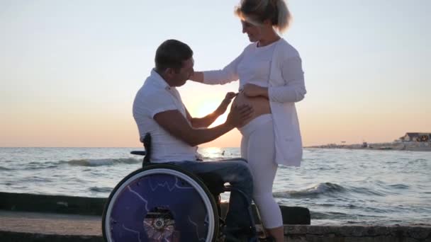 Crippled love, pregnant female with invalid husband in wheelchair at sunset, — Stock Video