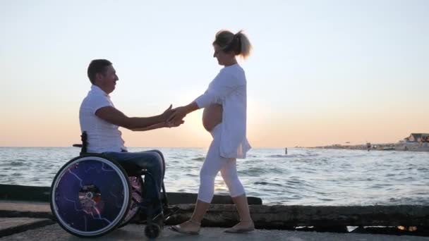 Schwangere bei Sonnenuntergang verkrüppelt: Behinderter streichelt Frau mit dickem Bauch an Böschung — Stockvideo