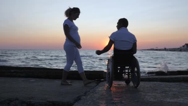 Behinderte und Frau heben abends die Hände, Behinderte mit schwangeren Mädchen beim Sonnenuntergang, erwartendes Baby, Ehemann — Stockvideo